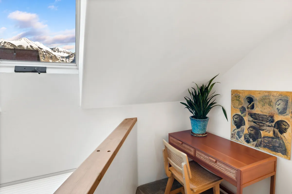 A serene interior scene featuring a desk by a window with lush mountain views, decorative plants, and inspiring artwork, suggesting a connection to the outdoors and a peaceful atmosphere for contemplation or planning daily adventures.