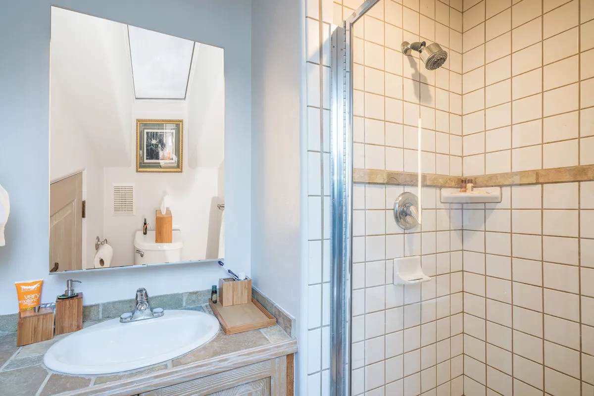 An inviting bathroom with a large mirror, modern sink, walk-in shower, and decorative art on the wall. The space feels fresh and serene, perfect for morning routines or a rejuvenating shower after a day outdoors.