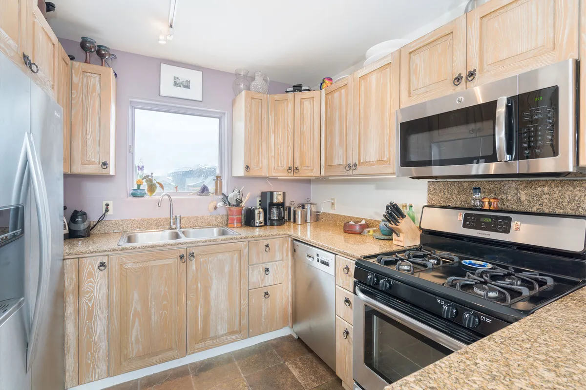A lively kitchen scene showcasing a spacious countertop, modern stainless steel appliances, and a window with a view. The area is designed for both family cooking and entertaining, with plenty of light and space for preparing meals together.