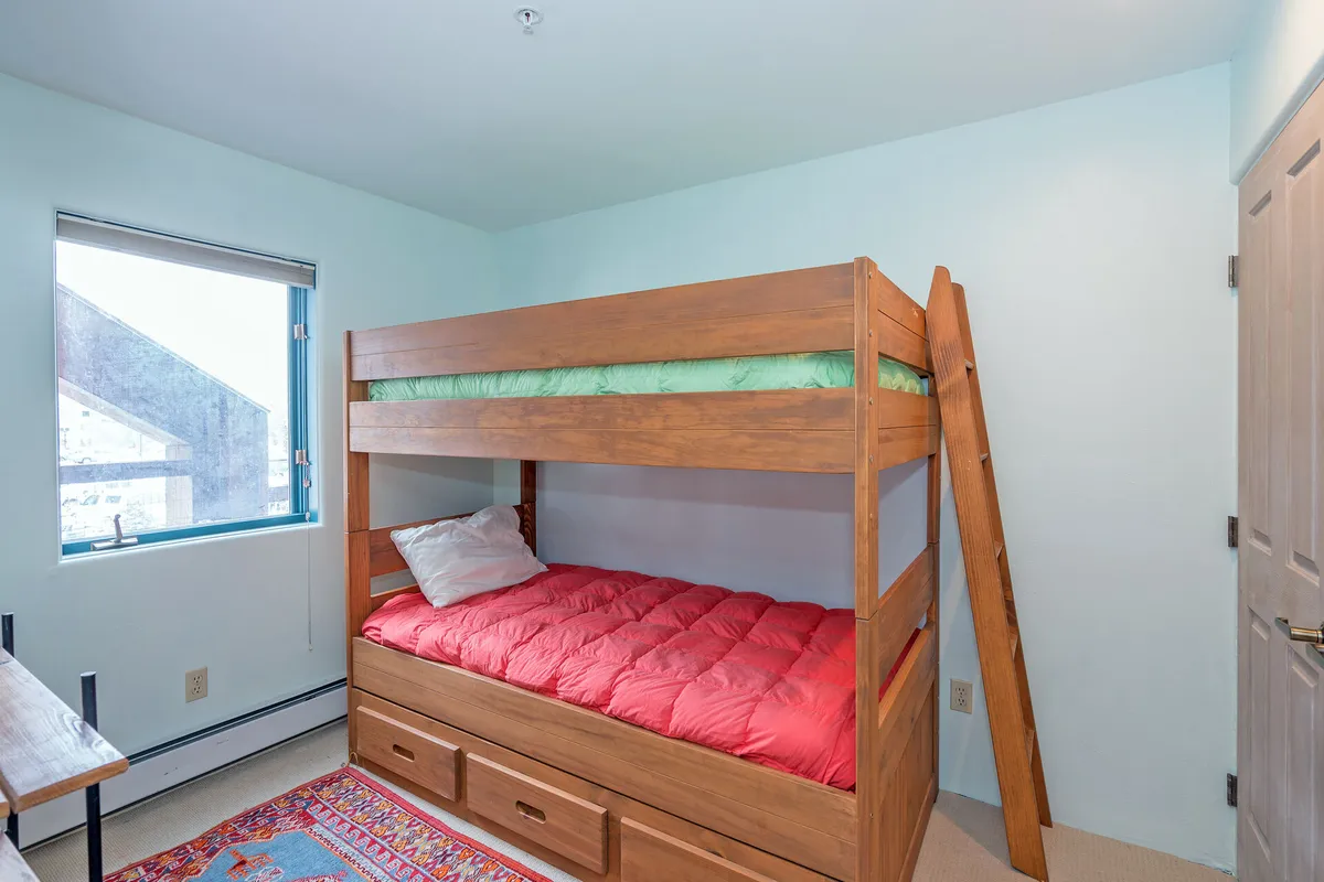 A cheerful bunk room with a sturdy bunk bed, colorful rug, and a window letting in plenty of morning light. The playful decor and cozy setup make this room inviting for kids or groups of friends, providing a fun and restful sleeping space.