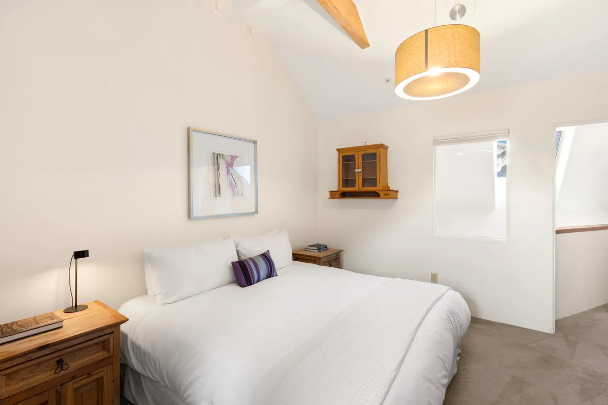 A soft, inviting queen bedroom with gentle natural light streaming in, tasteful artwork on display, and a wooden cabinet. The serene ambiance makes it ideal for restful nights and quiet mornings, reflecting a sense of privacy and comfort.
