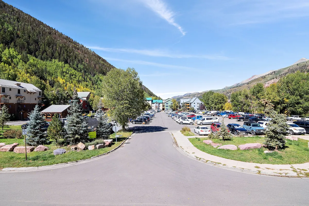 A welcoming exterior shot showcasing a mountain backdrop, a tree-lined street, clusters of vehicles, lush greenery, and distinctive rock formations. The vibrant autumn colors and community feel evoke the atmosphere of local events and festivals.