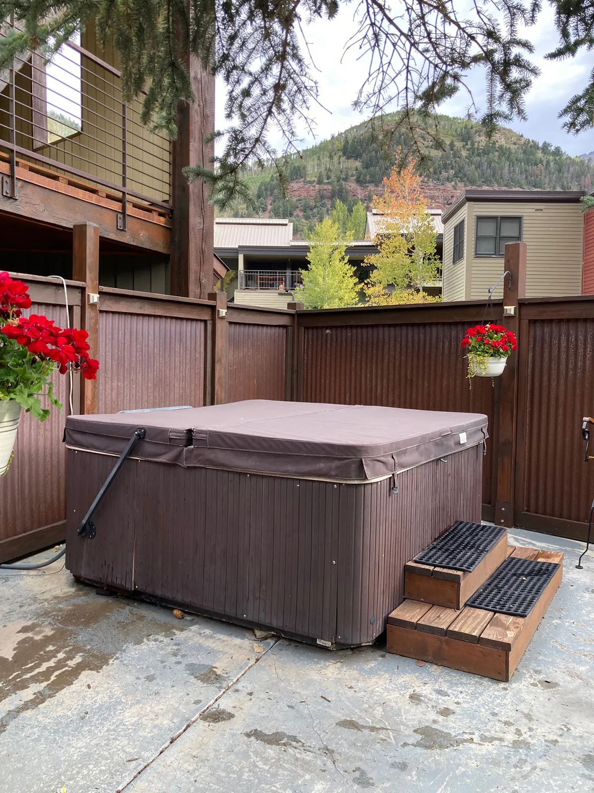 An inviting outdoor communal hot tub set against a stunning mountain backdrop, with flower pots adding a touch of color and nature to the tranquil scene. The image captures the relaxing, social atmosphere perfect for après-ski or unwinding after a day of adventure.