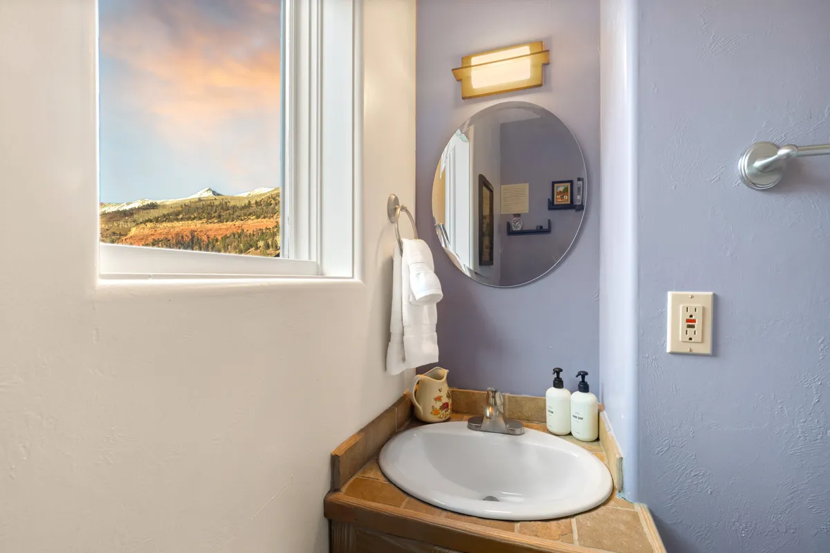 A bright interior bathroom space with a window framing scenic mountain vistas, a mirror, and a modern sink, evoking a sense of preparing for or unwinding after a day spent exploring.