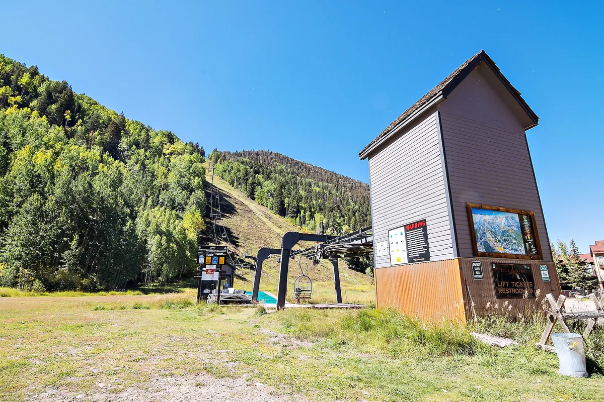 A dynamic exterior scene featuring a modern ski lift station at the base of a snowy mountain slope, with a visible ticket booth and open vista, ideal for showcasing immediate ski-in/ski-out access. The setting is lively and directly connects guests to the mountain adventure.