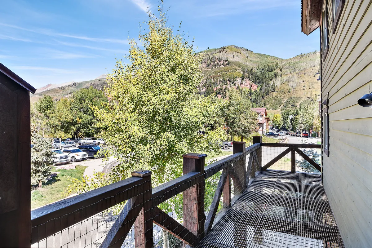 A tranquil balcony with a simple railing and a panoramic view of the mountains and a tree nearby. The outdoor atmosphere emphasizes the blend of privacy and immersion in nature, ideal for soaking in alpine air or sharing conversations as described in the section.